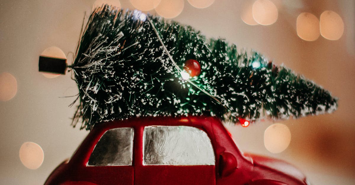 A red toy car carries a Christmas tree, set against a warm bokeh background, celebrating the festive season.