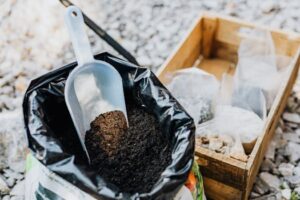 Close-up of gardening essentials with soil scoop, bag, and wooden box in garden setting.